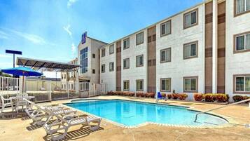 A hotel with a swimming pool, outdoor seating, and a covered area.