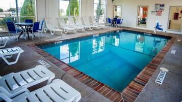 An indoor swimming pool with lounge chairs and a tiled floor.