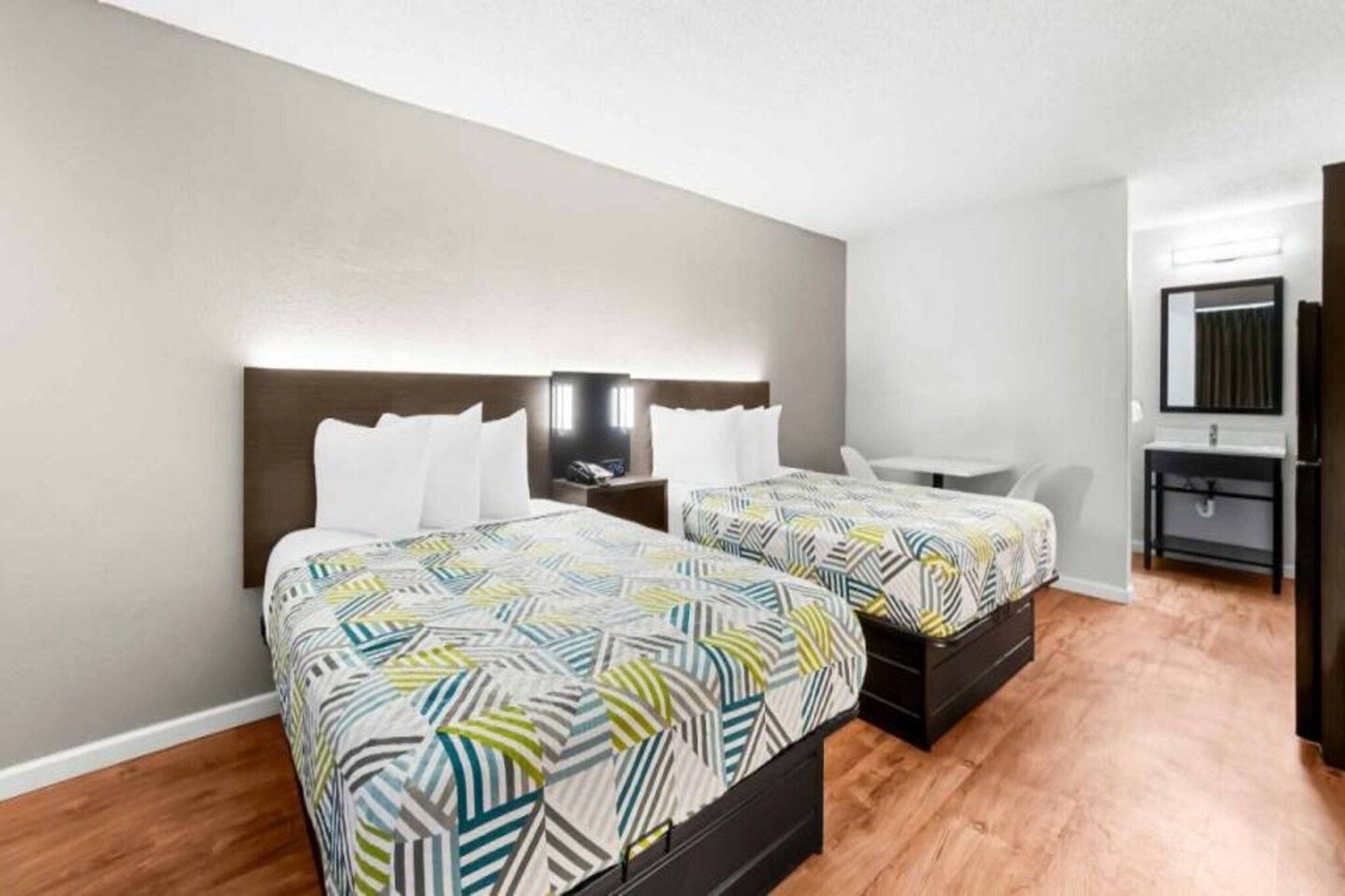 Une chambre d’hôtel avec deux lits, une table de chevet, un petit bureau, une chaise, un miroir et une salle de bain avec un lavabo et un miroir.