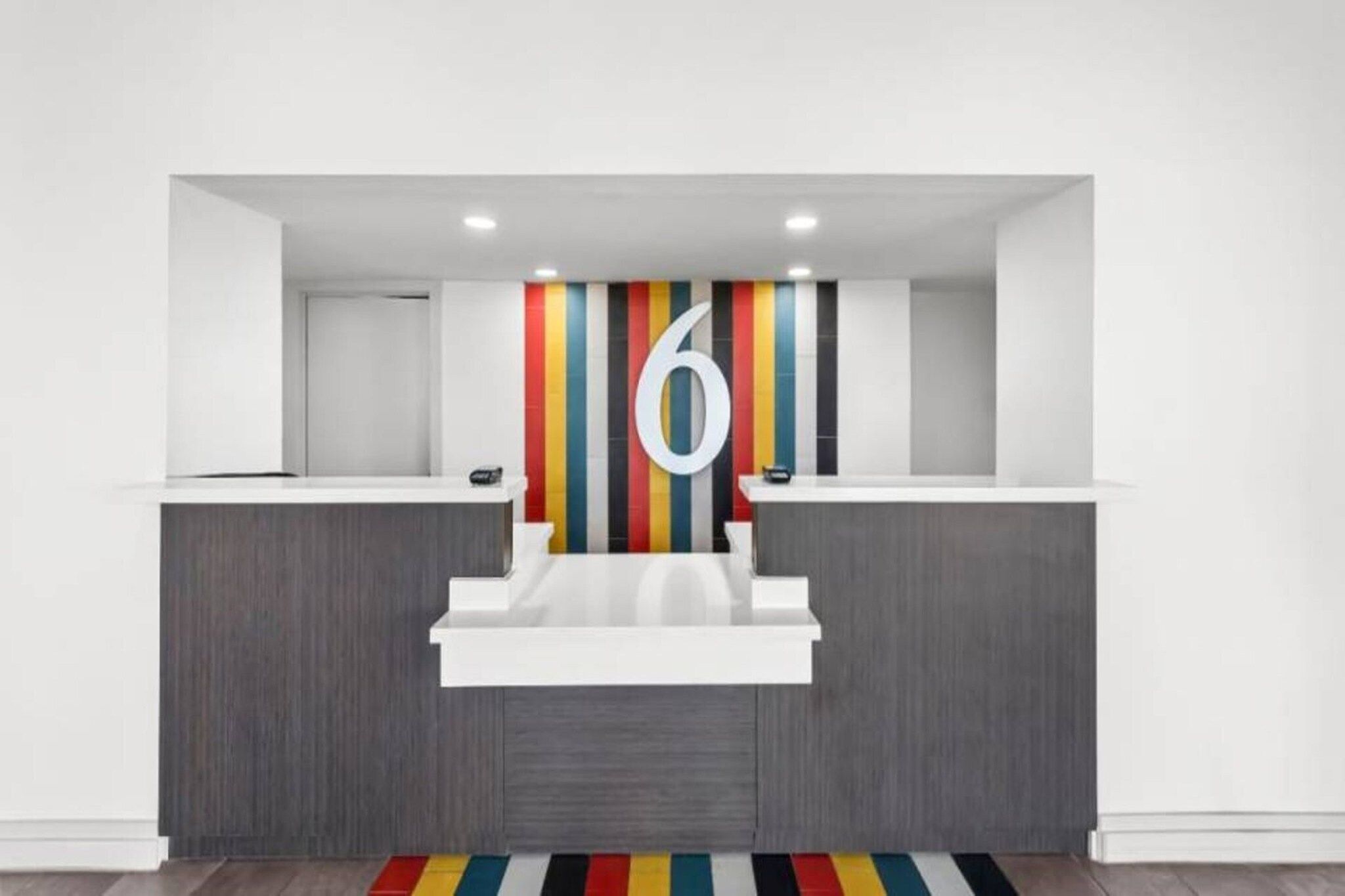 Un comptoir d’accueil avec un grand chiffre « 6 » affiché sur le mur, deux guichets et un mur rayé aux couleurs vives à l’arrière.