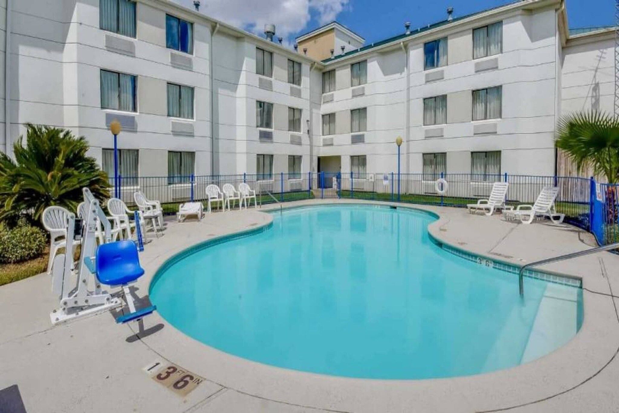 A swimming pool with lounge chairs and a building with multiple balconies.