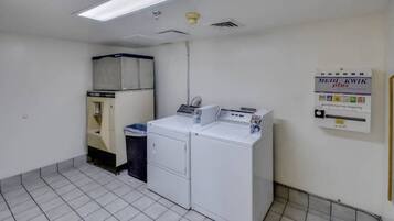 A laundry room with a washing machine, dryer, and a trash bin.