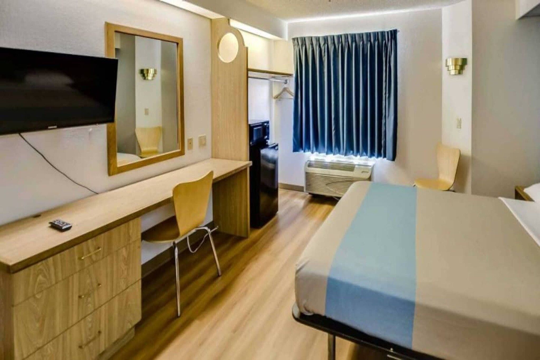 A hotel room with a bed, a desk, a chair, a television, and a window with curtains.