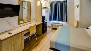 A hotel room with a bed, a desk, a chair, a television, and a window with curtains.