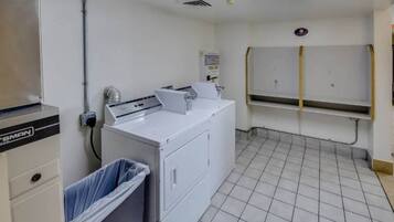 A laundry room with a washing machine, a dryer, and a trash bin.