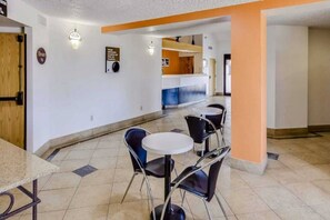 A hotel lobby with a reception desk, a seating area with tables and chairs, and a sign indicating the elevator location. - Spacious Queen Bed| Smoking (Katy)