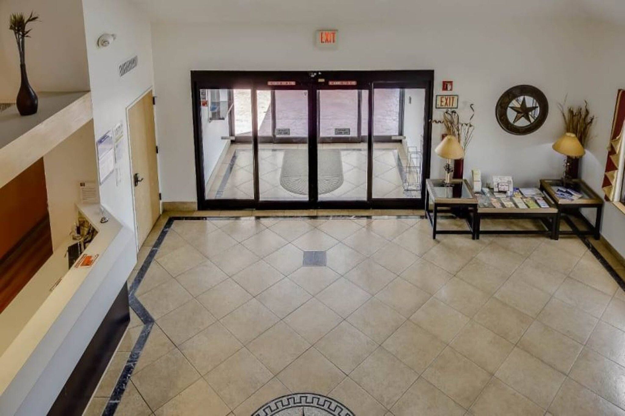 A hotel lobby with a reception desk, a coffee table, and an exit sign.