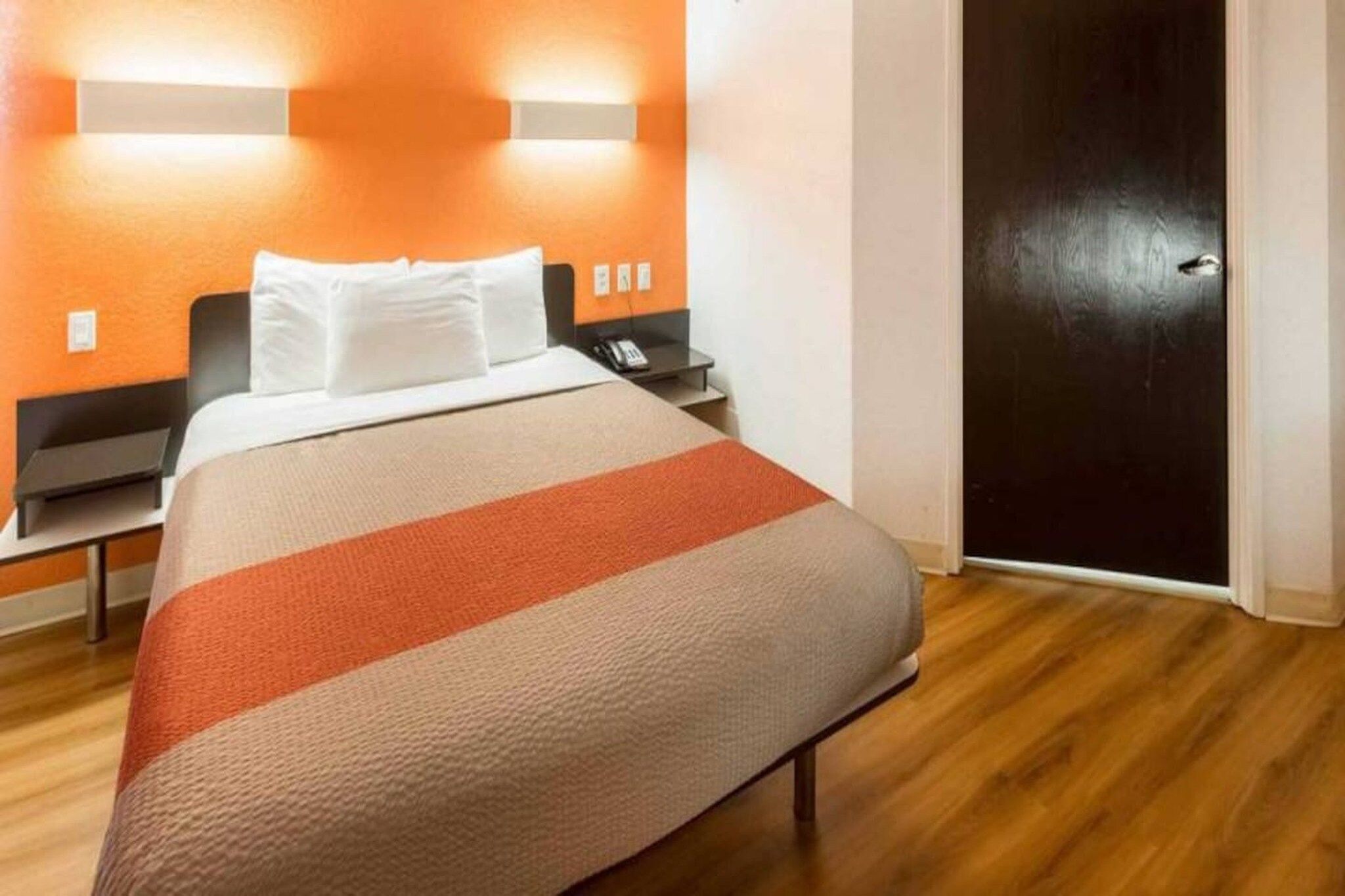 Una habitación de hotel con cama, mesita de noche y una puerta.