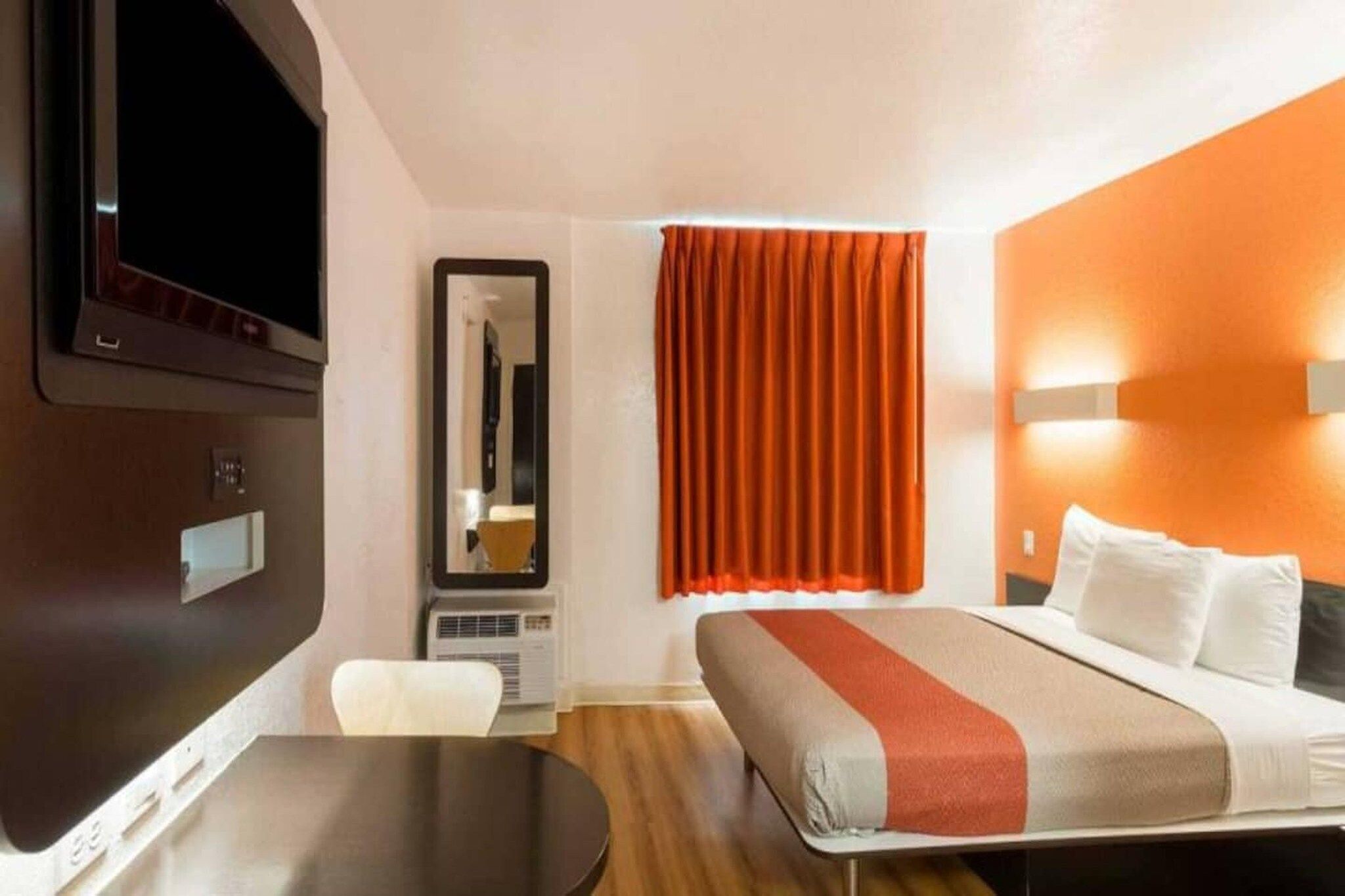 A hotel room with a bed, a desk, a chair, a television, a mirror, and a window with curtains.