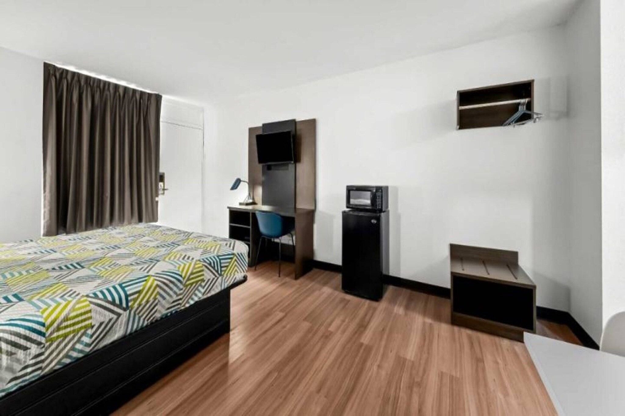 Ein Hotelzimmer mit Bett, Schreibtisch, Stuhl, Fernseher und einer kleinen Ablage.