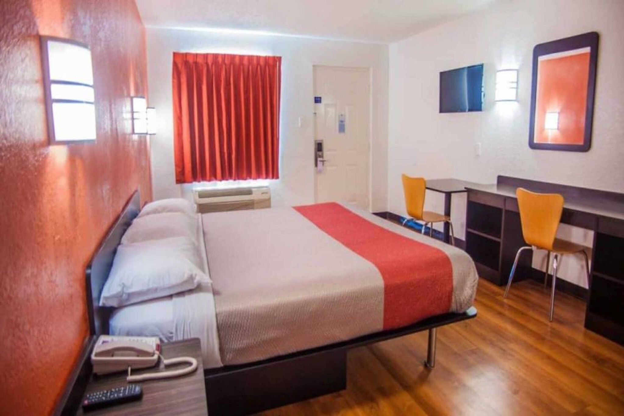 A hotel room with a bed, bedside table, and a desk with two chairs.