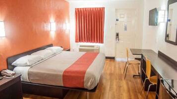 A hotel room with a bed, a desk, a chair, and a door.