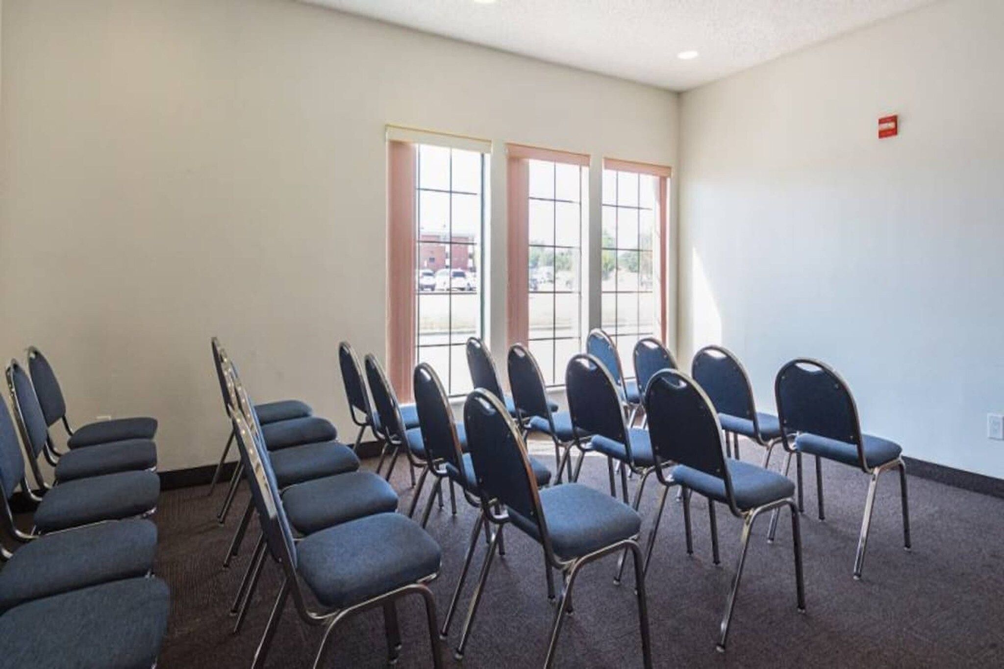 A conference room with rows of chairs, large windows, and a carpeted floor.