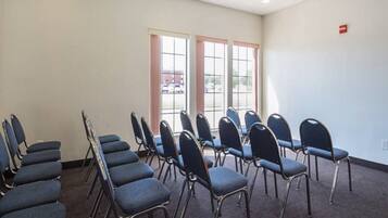 A conference room with rows of chairs, large windows, and a carpeted floor.