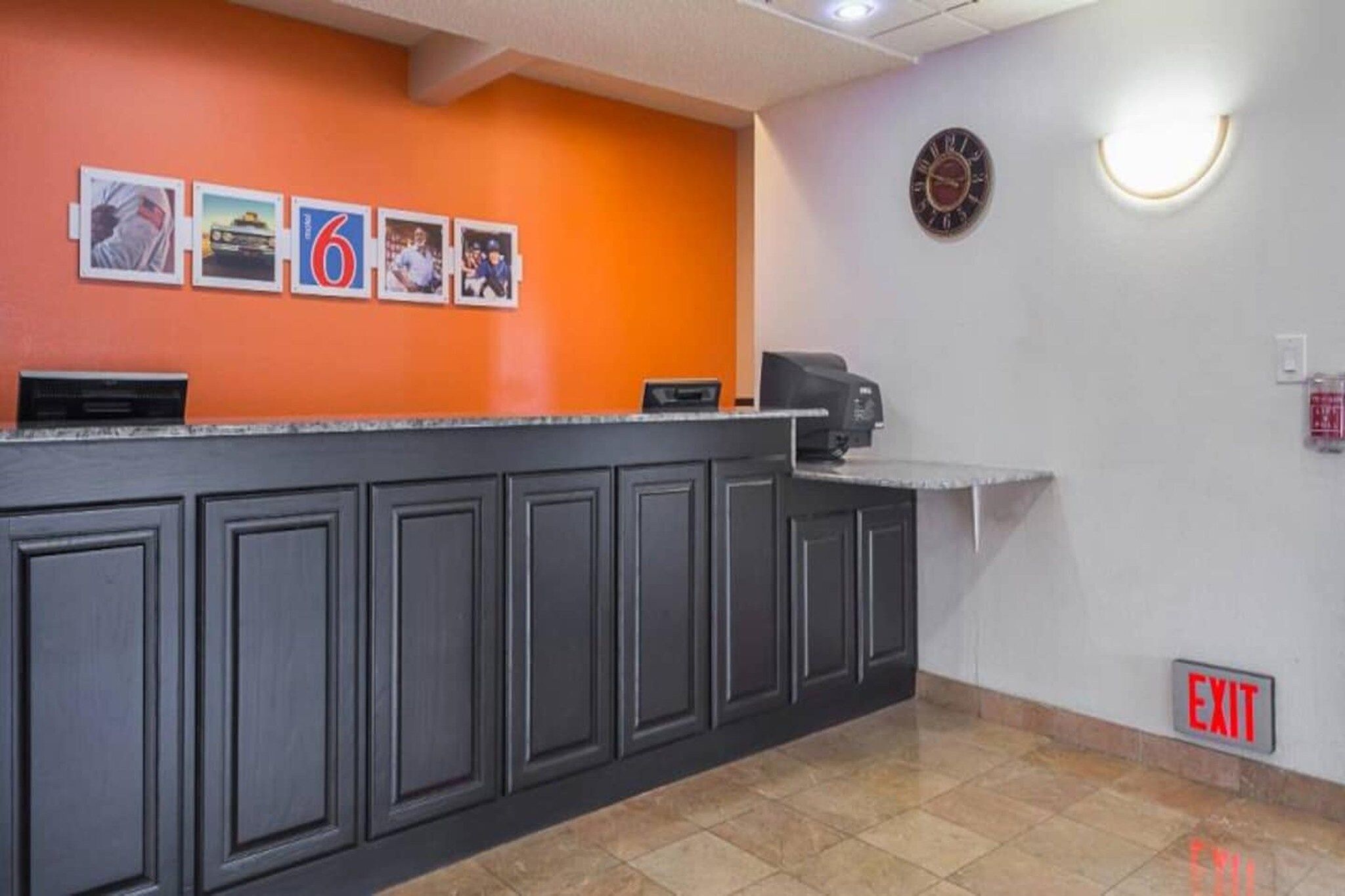 Un espace d’accueil avec un comptoir, des tableaux encadrés au mur, une horloge et un panneau indiquant la sortie.