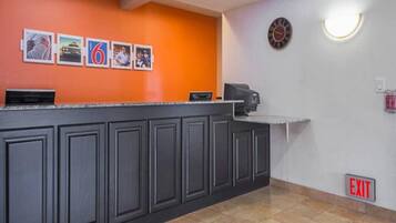 Un espace d’accueil avec un comptoir, des tableaux encadrés au mur, une horloge et un panneau indiquant la sortie.
