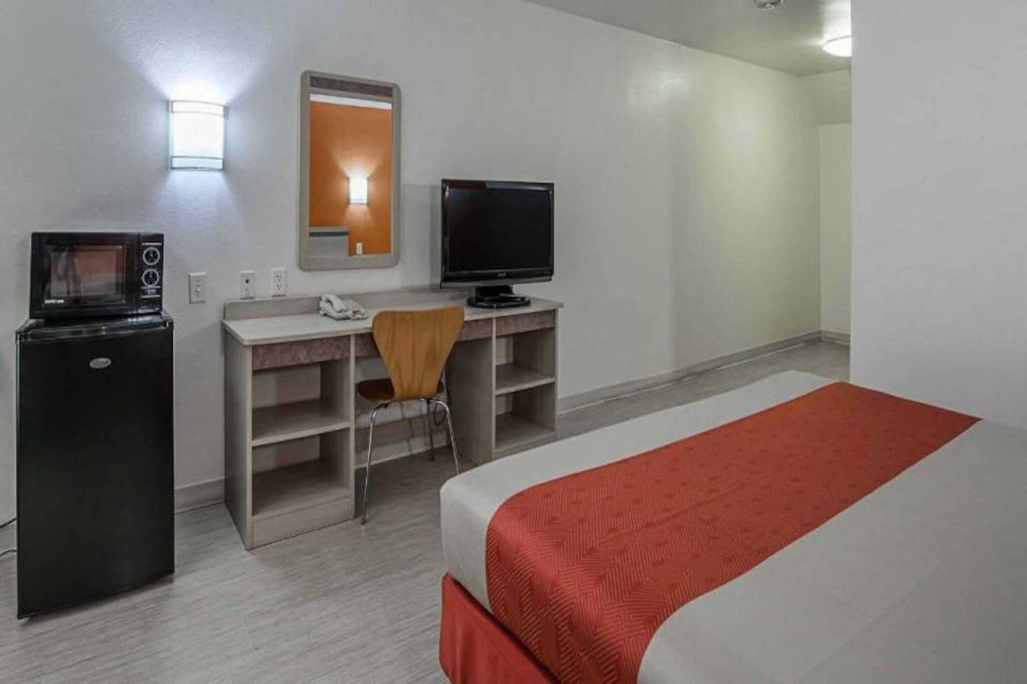 Habitación de hotel con cama, escritorio, silla, televisor, microondas y espejo.