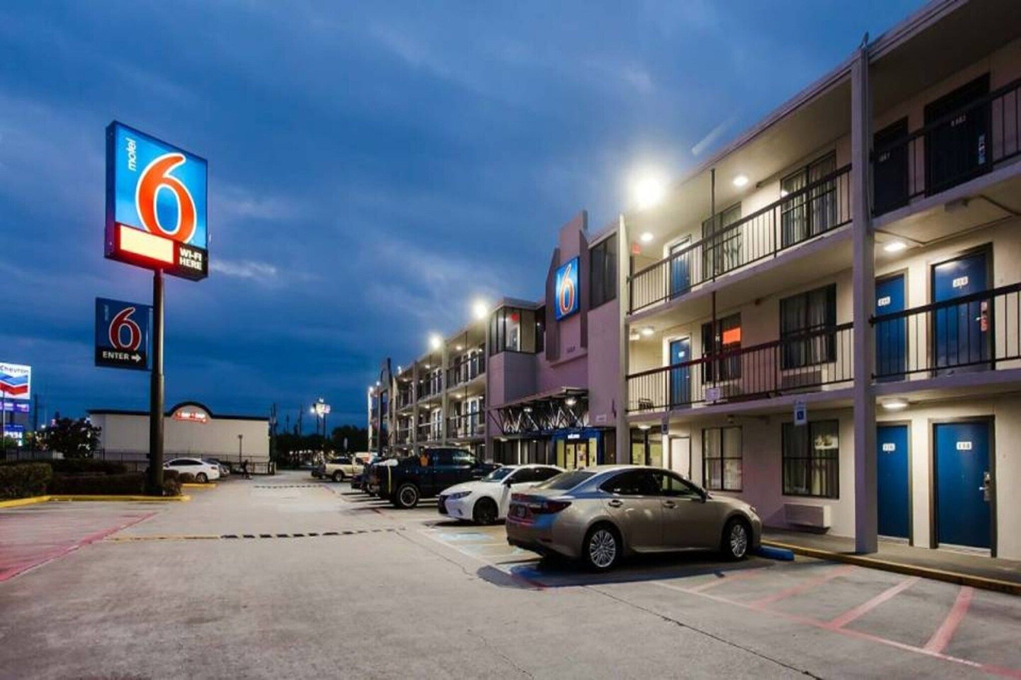 A motel with multiple floors, a parking lot with several cars, and illuminated signage.