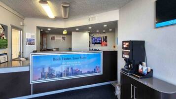 A reception area with a digital screen displaying a promotional message, a coffee machine, and a counter with a cityscape backdrop.