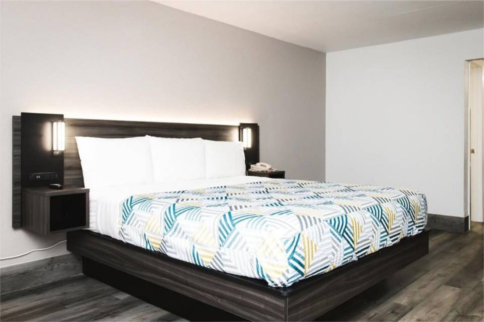 A modern bedroom with a wooden headboard, a bed with a patterned bedspread, bedside tables with lamps, and a nightstand with a phone.