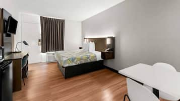 A modern hotel room with a bed, desk, chair, and a television.