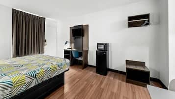 A hotel room with a bed, a desk, a chair, a television, and a small shelf.
