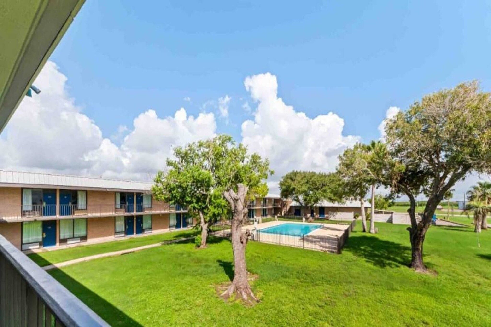 A hotel with a swimming pool, green lawn, and trees.