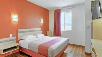 A hotel room with a bed, a chair, a desk, and a television.