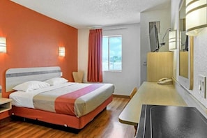 Una habitación de hotel con cama, escritorio, silla, ventana y espejo.