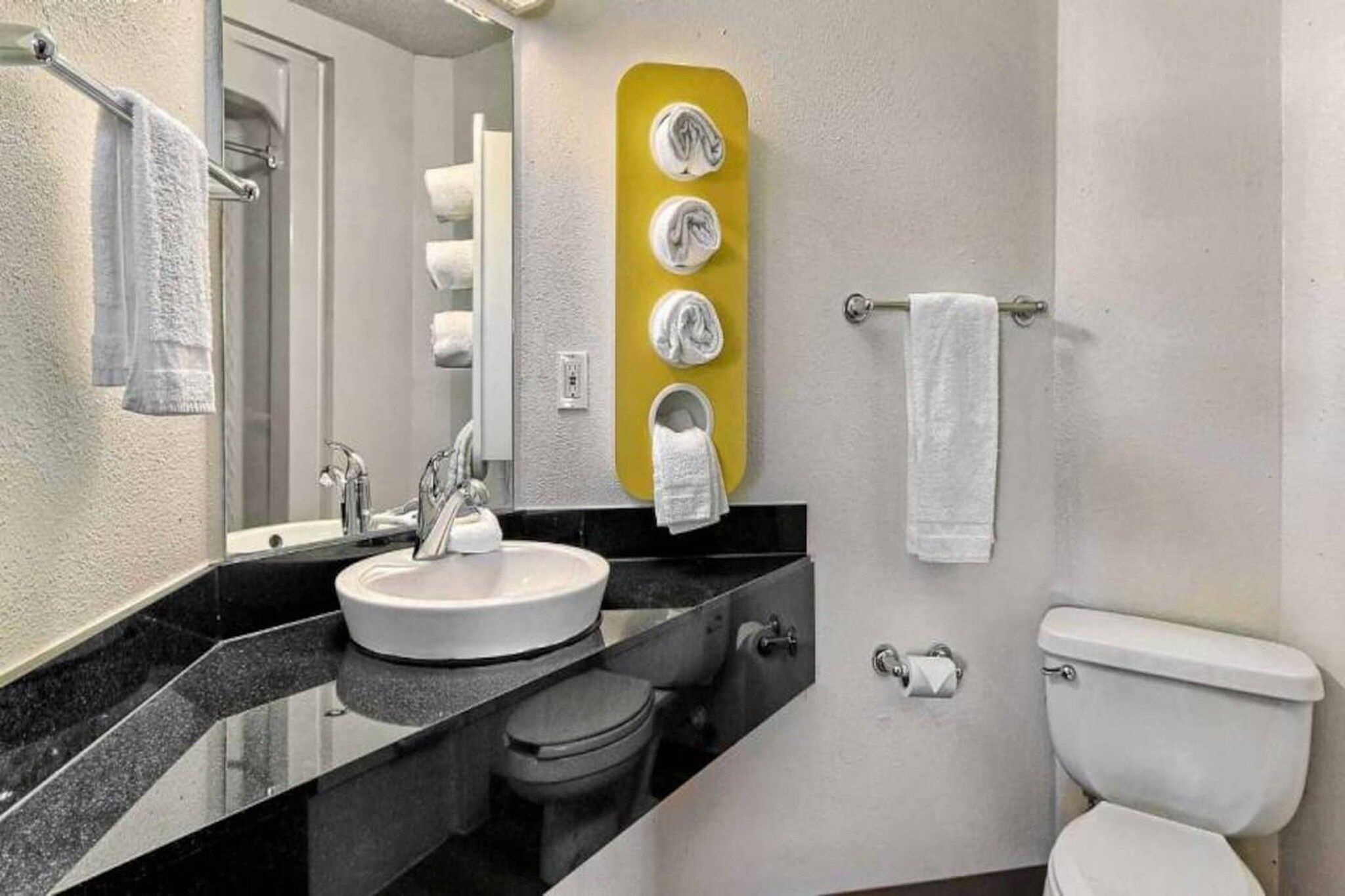 A bathroom with a sink, mirror, toilet, and towel rack.