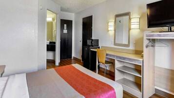 A hotel room with a bed, a desk, a chair, a television, and a wardrobe.