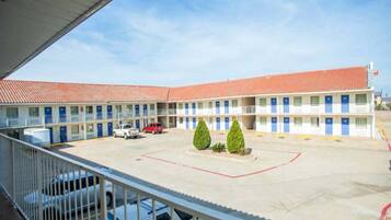 A motel with a central courtyard, multiple rooms with blue doors, and a red car parked in the lot.