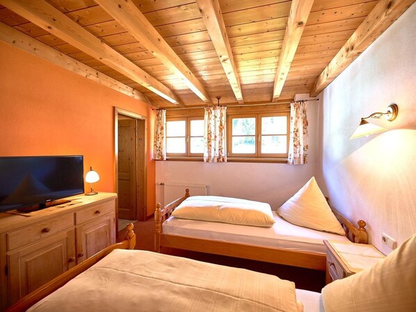 Ein Schlafzimmer mit zwei Betten, einem Fernseher, einem Schminktisch und einem Fenster mit Vorhängen.