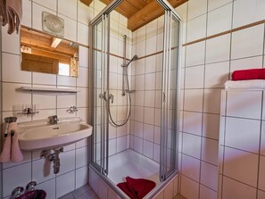 Ein Badezimmer mit einer gläsernen Duschkabine, einem Waschbecken mit Spiegel darüber und einem Handtuchhalter mit Handtüchern.