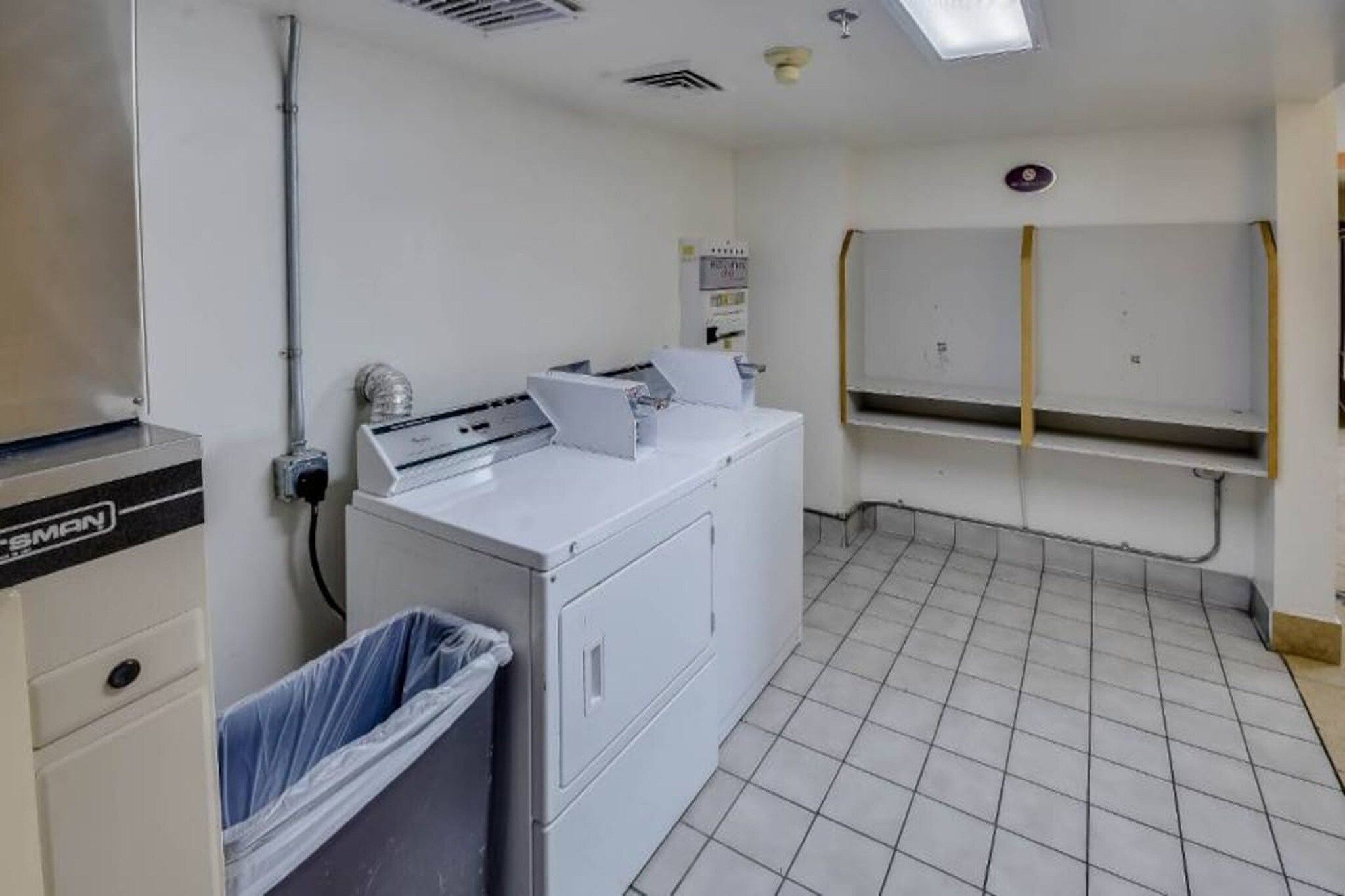 A laundry room with a washing machine, a dryer, and a trash bin.