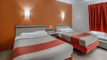 A hotel room with two beds, a window with red curtains, and a wall-mounted light fixture.