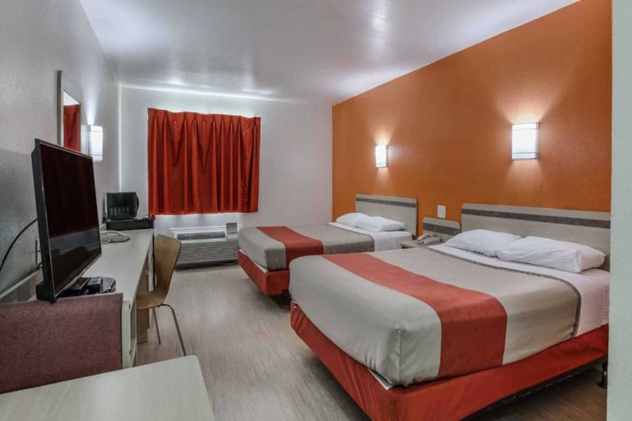 A hotel room with two beds, a desk, a chair, and a television.