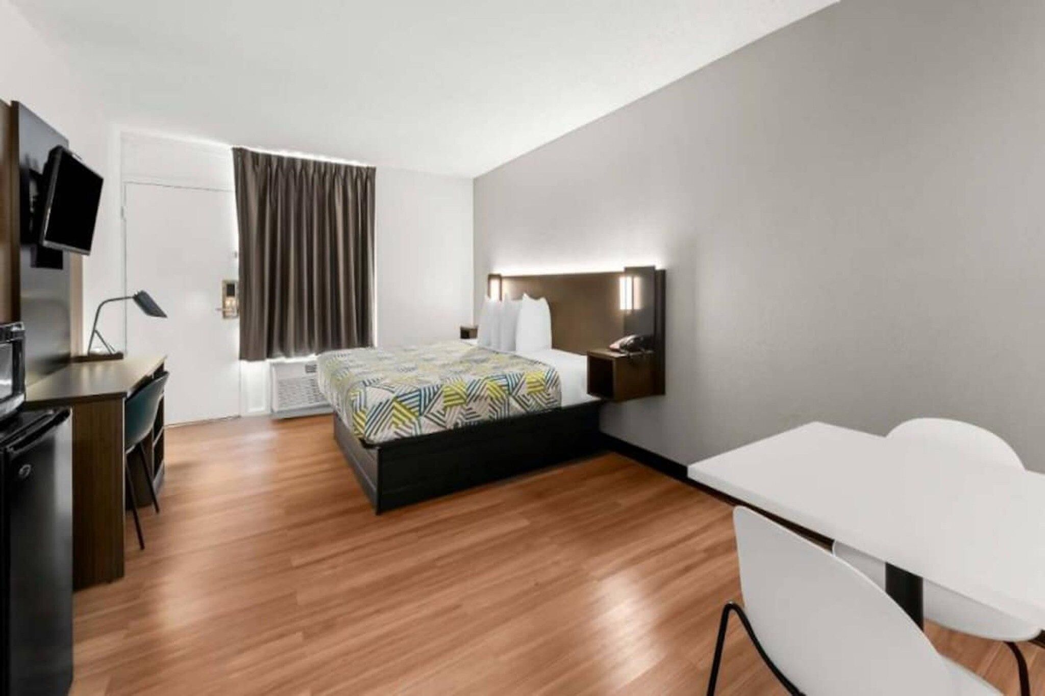 A modern hotel room with a bed, desk, chair, and a television.