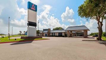 A 6 Hotel with a large sign, a parking lot, and a building with a covered area.