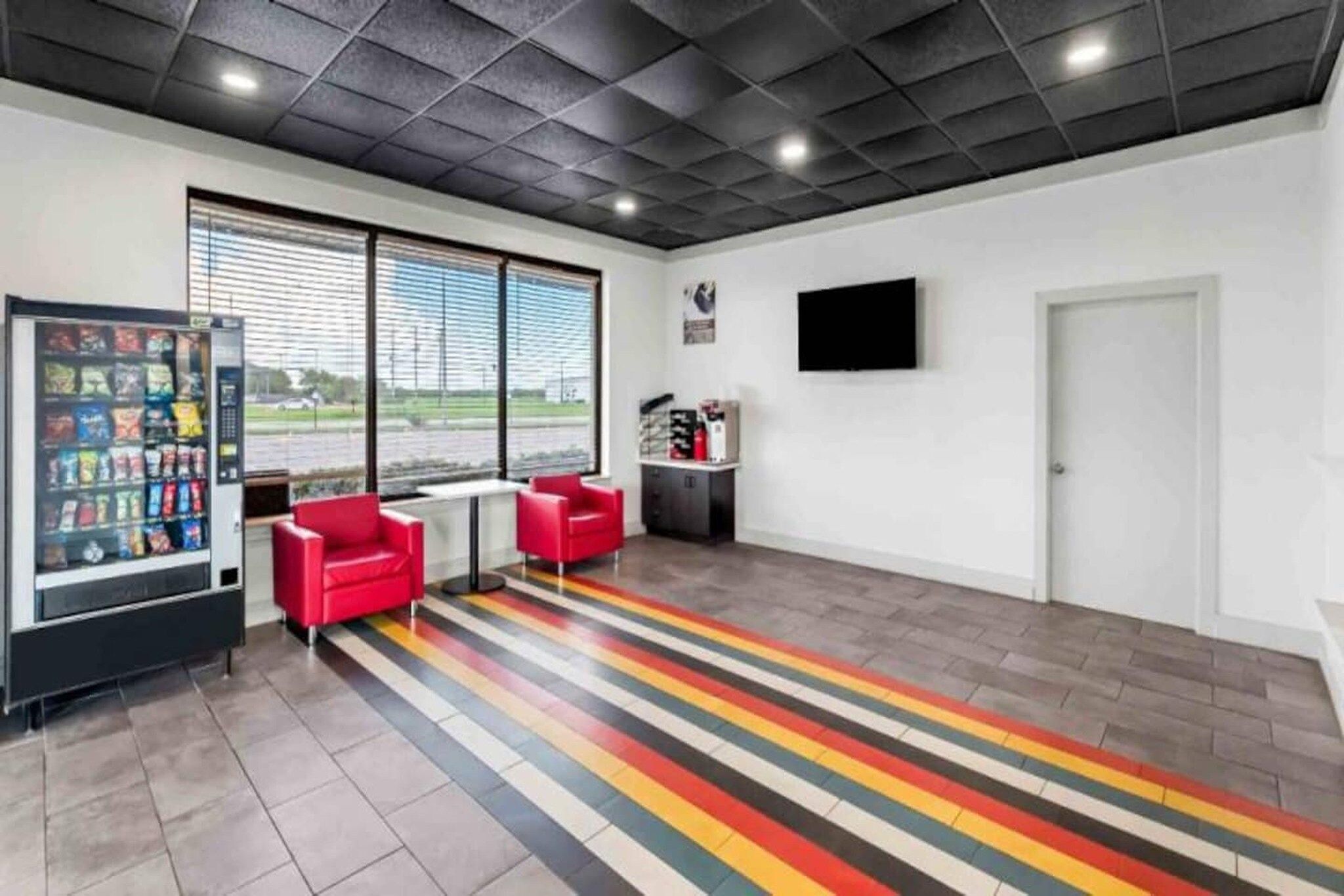 Un intérieur moderne avec un distributeur automatique, des chaises rouges, un téléviseur à écran plat et une porte.