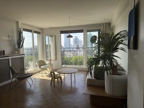 A spacious living area with a large window, a round table, and a potted plant. - Chic 75 m² Apartment with Views of the Canal and the Eiffel Tower (Paris)