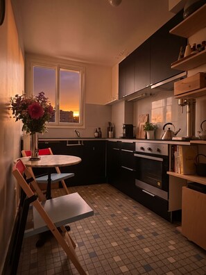 Cozinha compacta com área de refeições, janela com vista e piso ladrilhado.