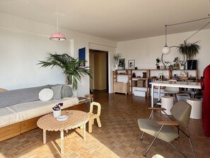 Uma sala de estar moderna com sofá, cadeiras, mesa de jantar e uma cozinha com prateleiras e plantas.