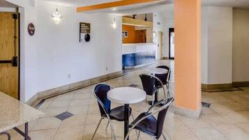 A hotel lobby with a reception desk, a seating area with tables and chairs, and a sign indicating the elevator location.