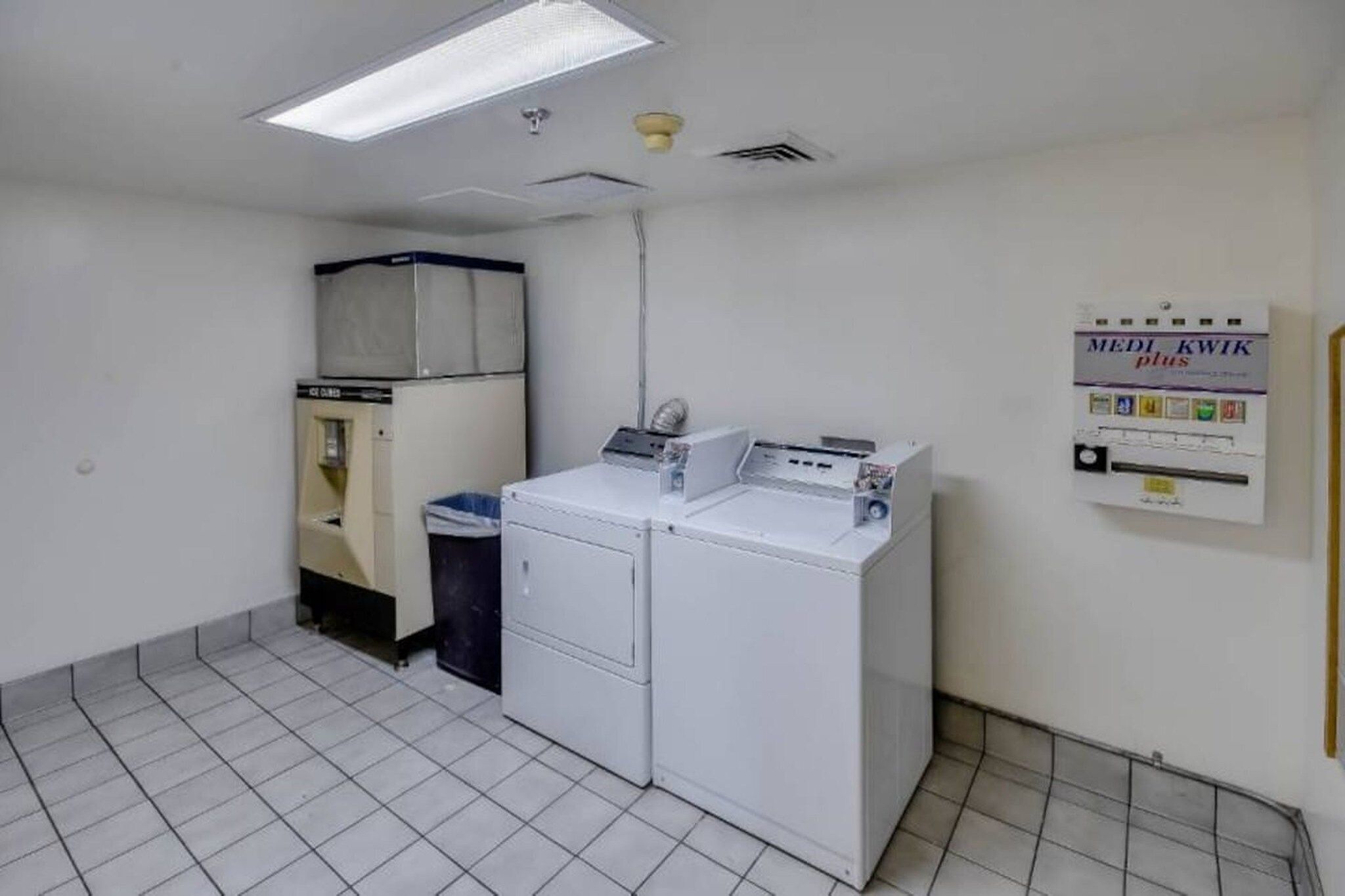 A laundry room with a washing machine, dryer, and a trash bin.