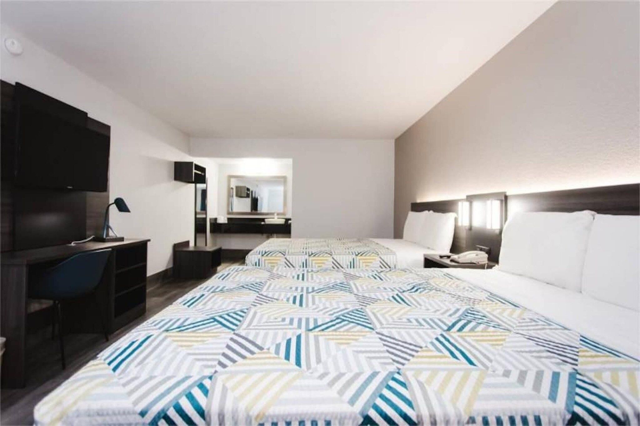 A hotel room with a bed, a desk, a chair, a TV, and a mirror.