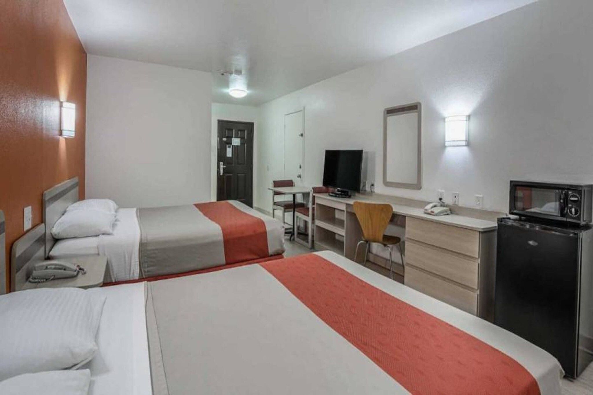 A hotel room with two beds, a desk with a computer, a television, and a microwave.
