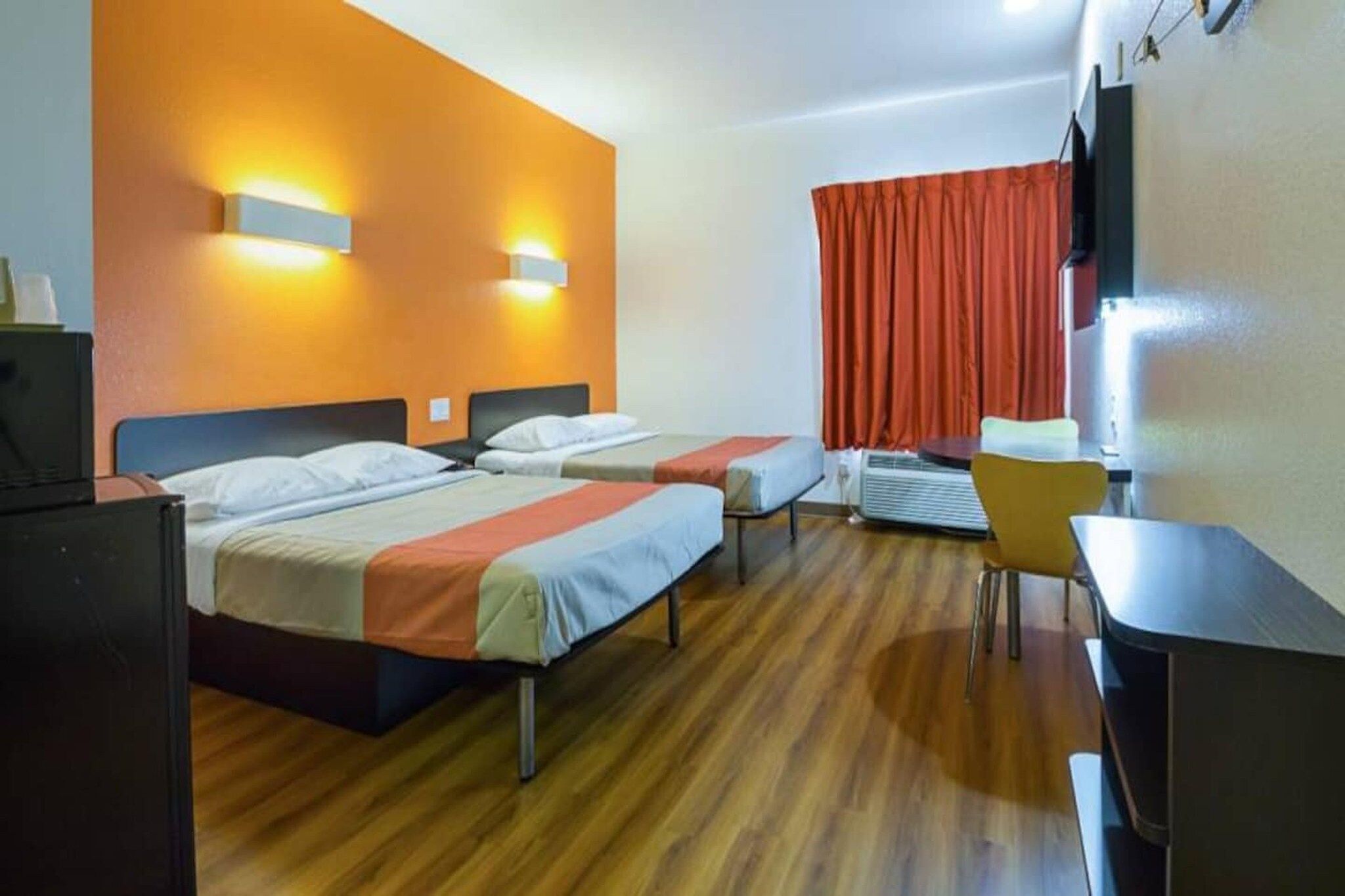 A hotel room with two beds, a desk, a chair, and a television.