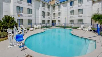A swimming pool with lounge chairs and a building with multiple balconies.
