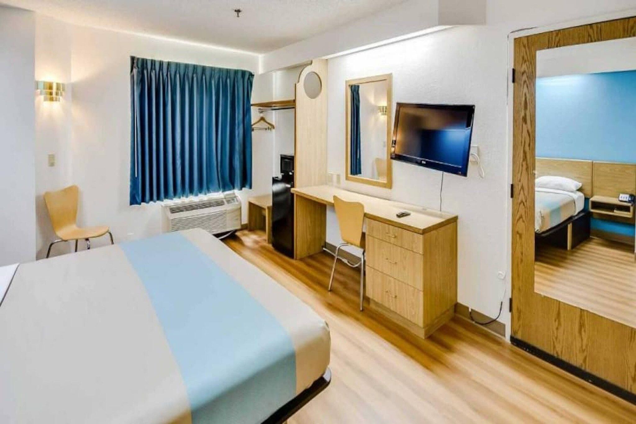 Habitación de hotel con cama, escritorio, silla, televisor y espejo.